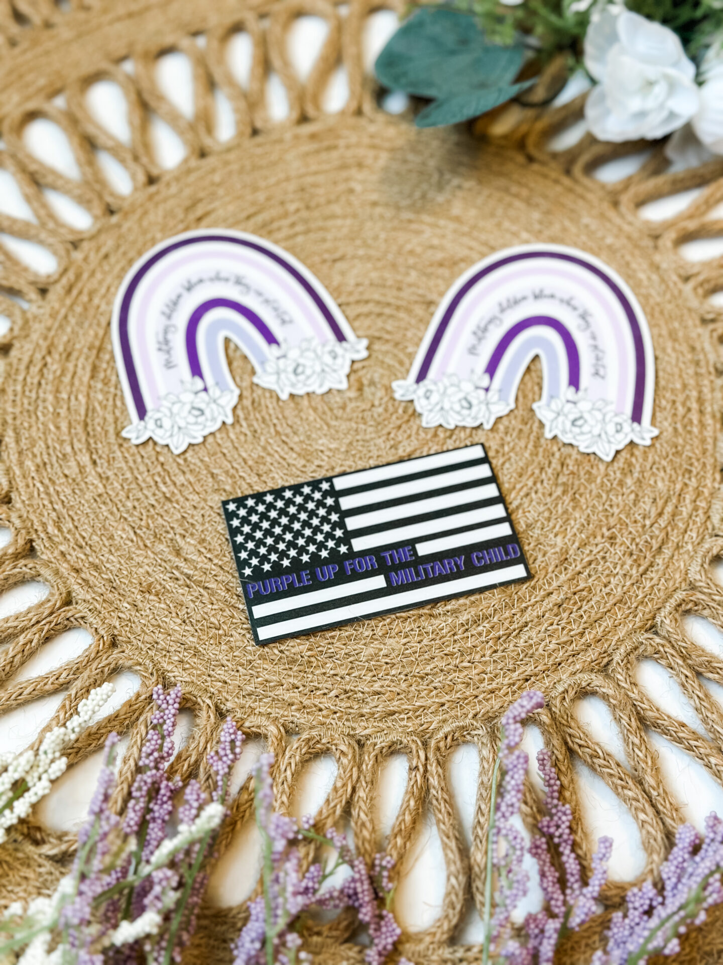 Waterproof stickers featuring a rainbow and floral design saying, “Military children bloom where they are planted” and a black and white flag design saying, “Purple up for the military child”