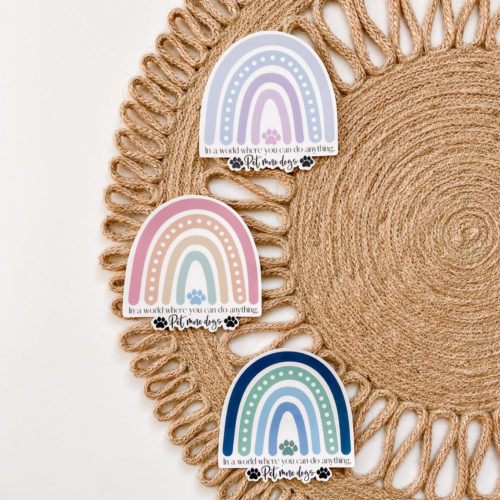 Handmade water-resistant sticker featuring a rainbow in a variety of colors, and the saying, “In a world where you can do anything, pet more dogs.”