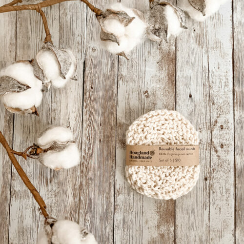 A set of Virginia-grown cotton reusable facial rounds rests on a wood floor, with a cotton stem surrounding the set on the top and left